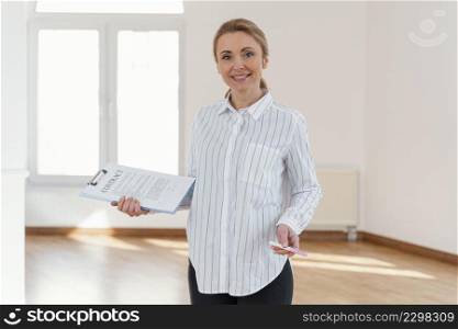front view smiley female realtor empty house holding clipboard