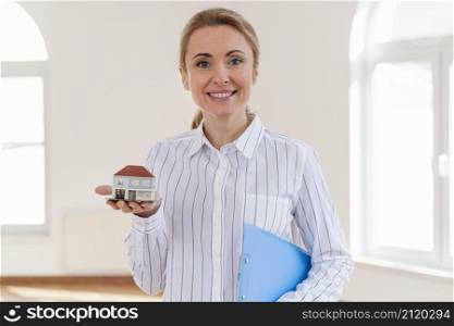 front view smiley female realtor holding miniature house