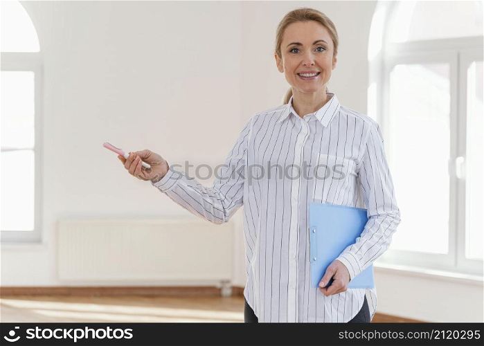 front view smiley female realtor with clipboard empty house