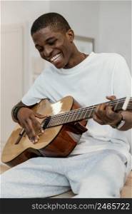 front view smiley male musician home playing guitar