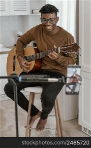 front view smiley male musician home playing guitar recording with smartphone
