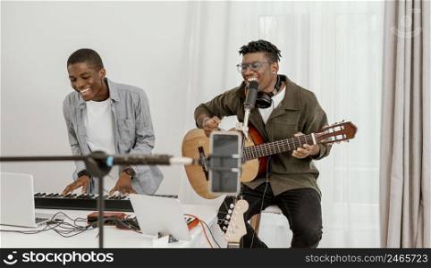 front view smiley male musicians home playing electric keyboard guitar