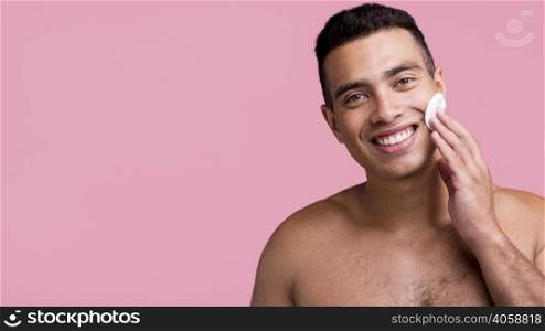 front view smiley shirtless man using cotton pads his face