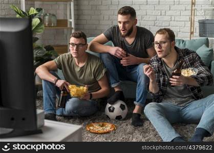 front view three male friends watching sports tv together while having snacks beer