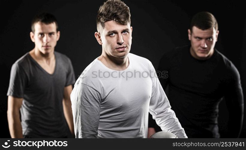 front view three male rugby players posing with ball