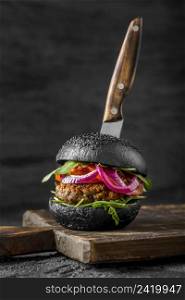 front view veggie burger with black buns cutting board with knife