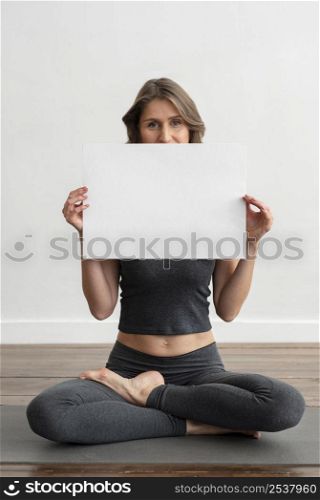 front view woman holding blank placard while doing yoga