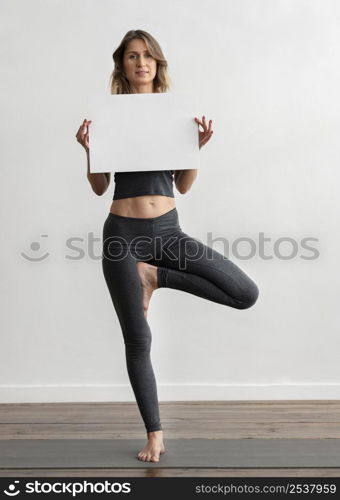 front view woman holding blank placard while doing yoga home