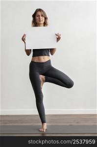 front view woman holding blank placard while doing yoga home