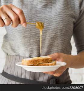 front view woman pouring honey ober bread slice