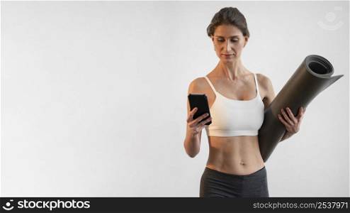 front view woman using smartphone while holding yoga mat with copy space