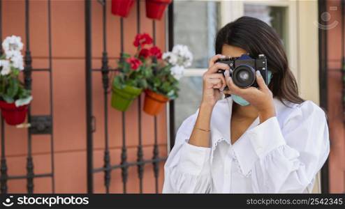 front view woman with face mask using camera outdoors