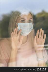 front view woman with medical mask home touching window during pandemic
