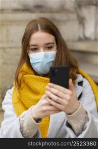 front view woman with medical mask taking pictures with smartphone