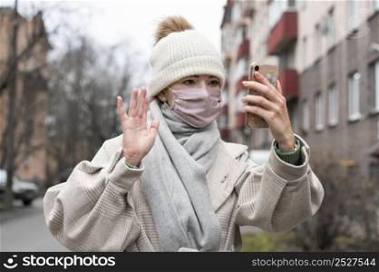 front view woman with medical mask waving smartphone