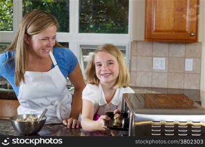 Front view, young girl looking forward, of mother and her young daughter putting raw cookie dough into portable oven