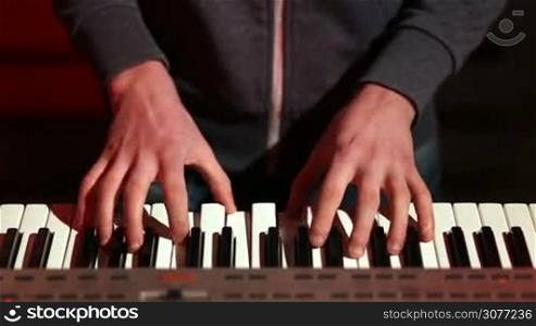 Frontal view of musician hands playing digital piano on stage in colorful spotlights while band performing song. High angle. Closeup of male hands playing synthesizer keyboard during rehearsal.