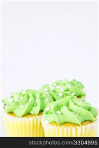 Frosting in spring&rsquo;s light green tops vanilla cupcakes placed in the bottom of a vertical frame with copy space above; focus placed on front cupcake of three;