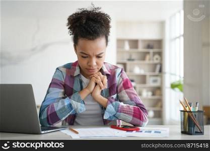 Frowning mixed race teen girl student learning, doing homework, sitting at desk with laptop. Focused teenager schoolgirl solves difficult task, preparing for exam. Stress and education concept.. Mixed race girl student solves task, preparing for exam at desk with laptop. Stress and education