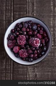 Frozen berries mix in a black bowl on wooden background. Still life photography