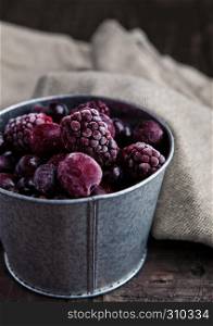 Frozen berries mix in a black bowl on wooden background. Still life photography