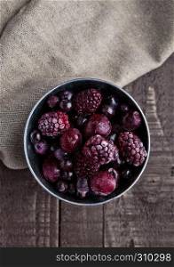 Frozen berries mix in small steel bucket on wooden table. With kitchen towel