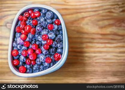 Frozen blueberries and cranberry in a gray cup on wooden background closeup. Space for copy.. Blueberries And Cranberry In A Cup