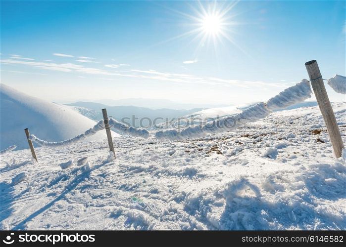 Frozen fence with ice and snow in winter alpine village. Mountain landscape