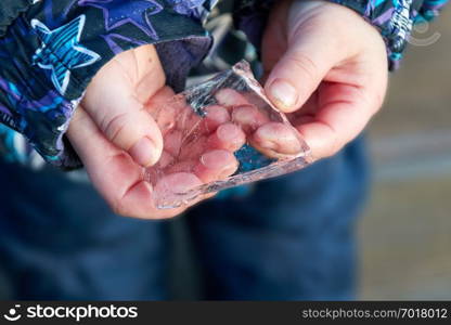 frozen ice, a clear, fresh, cold and transparent ice shard in the hands of a child. frozen ice in the hands of a child