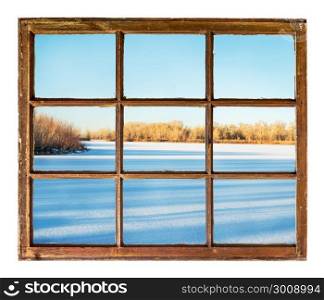 frozen lake with long tree shadows as seen through vintage, grunge, sash window with dirty glass