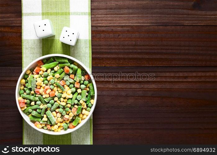 Frozen mixed vegetables (green bean, pea, carrot, sweet corn) in bowl, photographed overhead on dark wood with natural light. Frozen Mixed Vegetables