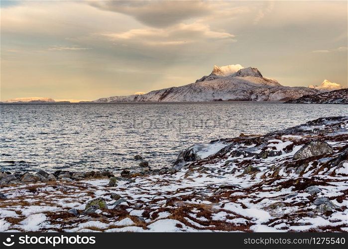 Frozen tundra landscape with cold greenlandic sea and snow Sermitsiaq mountain in the background, nearby Nuuk city, Greenland