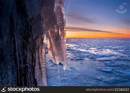 Frozen water as ice, created by wind and waves at the dutch shore throughout the winter. Ice sculpture mooring post during sunset in winter at the Afsluitdijk in The Netherlands