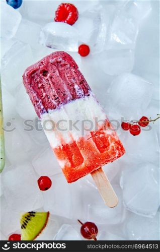 Frozen yogurt or ice cream with watermelon, and blueberries over ice with berries, healthy summer dessert.. Tricolor fruit and berries ice cream on wooden stick over ice with berries, top view