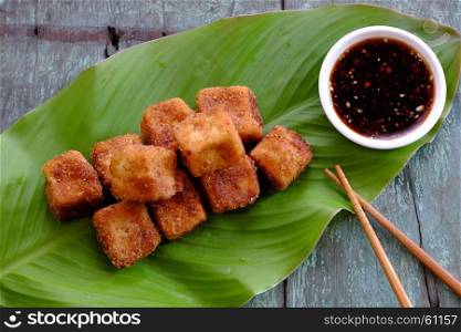 Frugal vegetarian food from Vietnamese cuisine, fried tofu with spice power, cover with crispy flour, homemade food on green leaf background, soya sauce for vegan