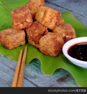 Frugal vegetarian food from Vietnamese cuisine, fried tofu with spice power, cover with crispy flour, homemade food on green leaf background, soya sauce for vegan