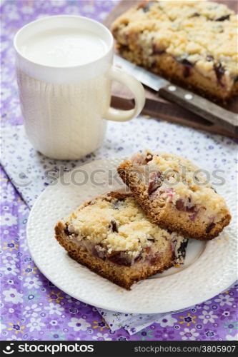 Fruit cake with streusel on plate with cop of milk, selective focus