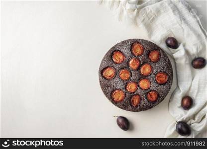 Fruit dessert, a plum tart with chocolate on a white background and kitchen towel. Above view of a plum pie. Flat lay with autumn sweet food.