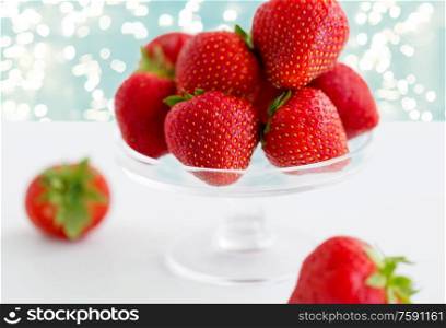 fruit, food and berries concept - strawberries on glass stand over lights on blue background. strawberries on glass stand over white background