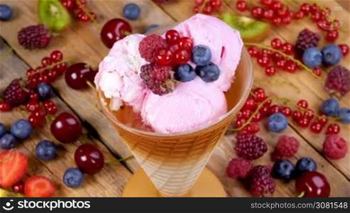 Fruit ice cream in cup rotating on wooden table full of summer forest fruits.