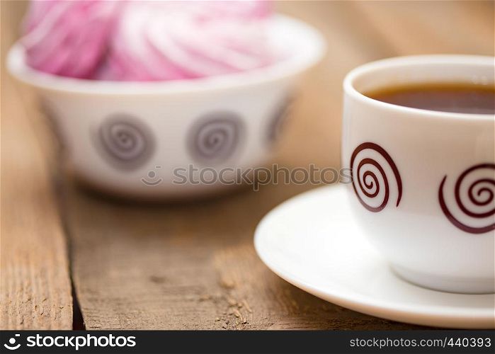 fruit marshmallows and the cup of tea on a wooden background