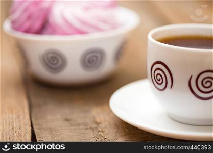 fruit marshmallows and the cup of tea on a wooden background