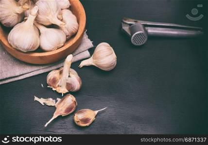 Fruit of garlic in a wooden bowl and on a table, black wooden background