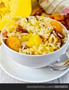Fruit Pilaf with pumpkin, raisins, dried apricots in a bowl, napkin, pumpkins, dried fruit, napkin, spoon on a wooden boards background