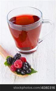 Fruit red tea with wild berries in wooden spoon on white wooden table