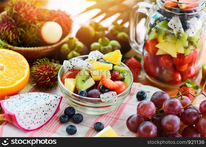 Fruit salad bowl fresh summer fruits and vegetables healthy organic food strawberries orange kiwi blueberries dragon fruit tropical grape tomato lemon rambutan pineapple background