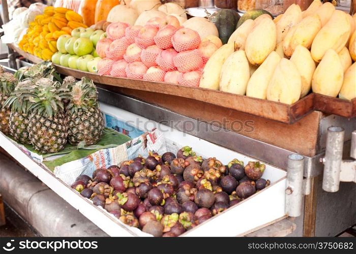 Fruit stalls in the market, pineapple, mango, apple, available for purchase.