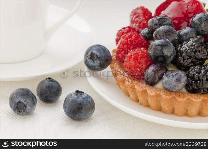 fruit tart with blueberry, blackberry, raspberry and strawberry, a coffee cup in background