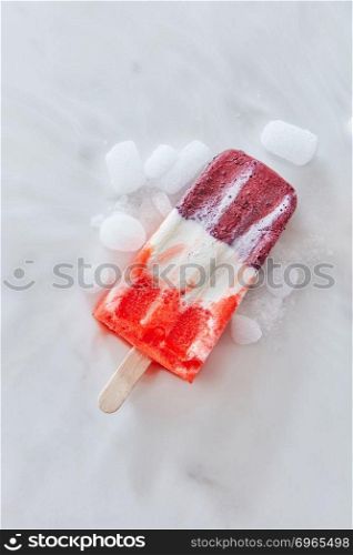 Fruit vanilla ice cream popsicle with ice slices is represented on a gray concrete background with space for text. Flight cold dessert. Top view. Vanilla berry sorbet on a stick with ice slices on a gray marble background with copy space. Top view