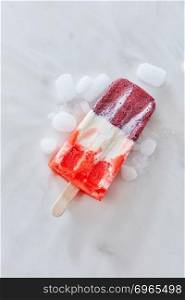Fruit vanilla ice cream popsicle with ice slices is represented on a gray concrete background with space for text. Flight cold dessert. Top view. Vanilla berry sorbet on a stick with ice slices on a gray marble background with copy space. Top view